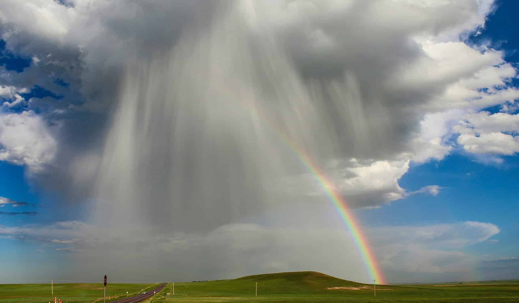 A dramatic rainstorm gives way to a rainbow over farmland, photo by NOAA