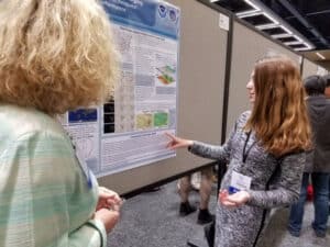 A young woman presents a science poster at a conference