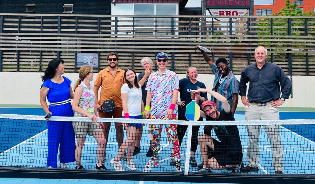 Riverside employees gathered together for a fun game of pickleball wearing playful outfits and goofing around